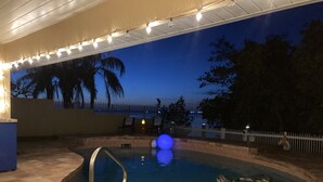 An outdoor swimming pool with a diving board, surrounded by a white fence, and a view of the ocean at dusk. - Beautiful River Front Home - Private Pool - Walk to Beach-Kayaks (Cocoa Beach)