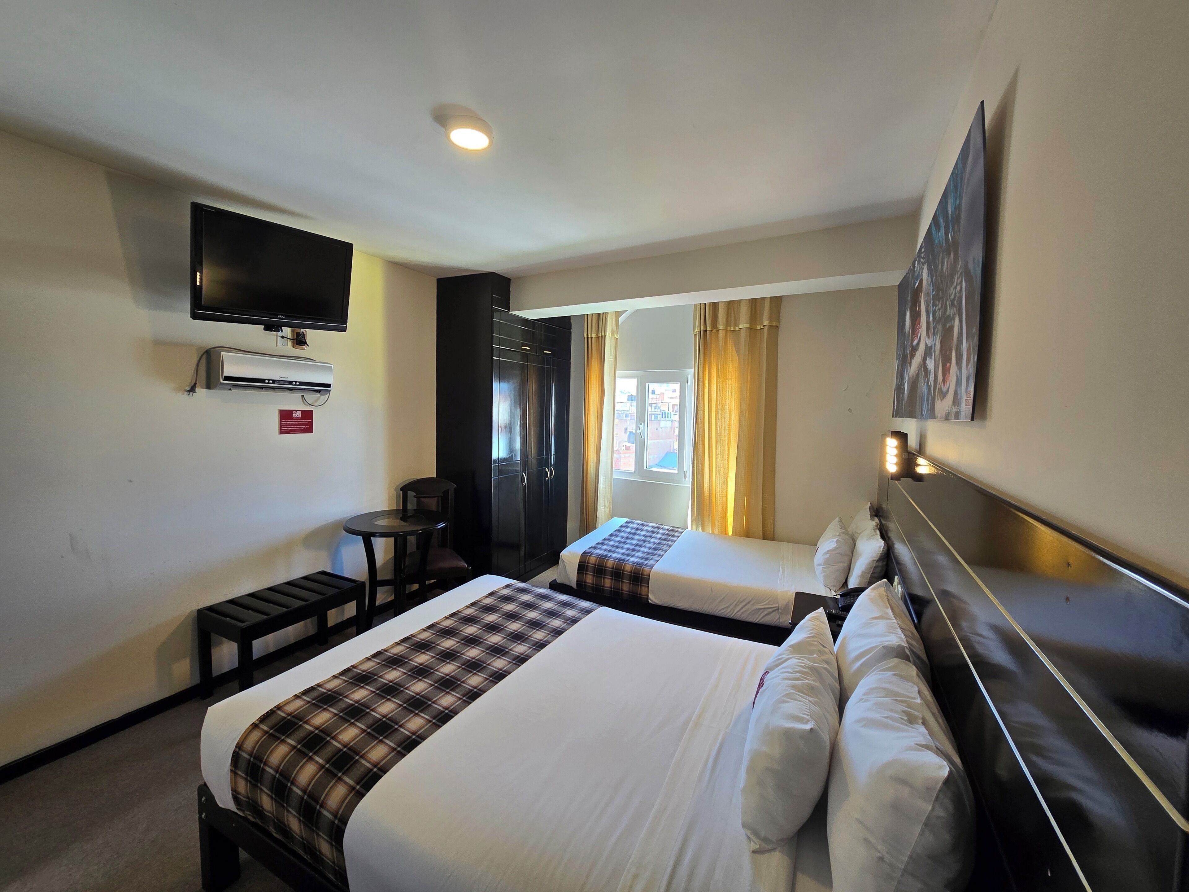 A hotel room with two beds, a TV, a desk, and a window with curtains.