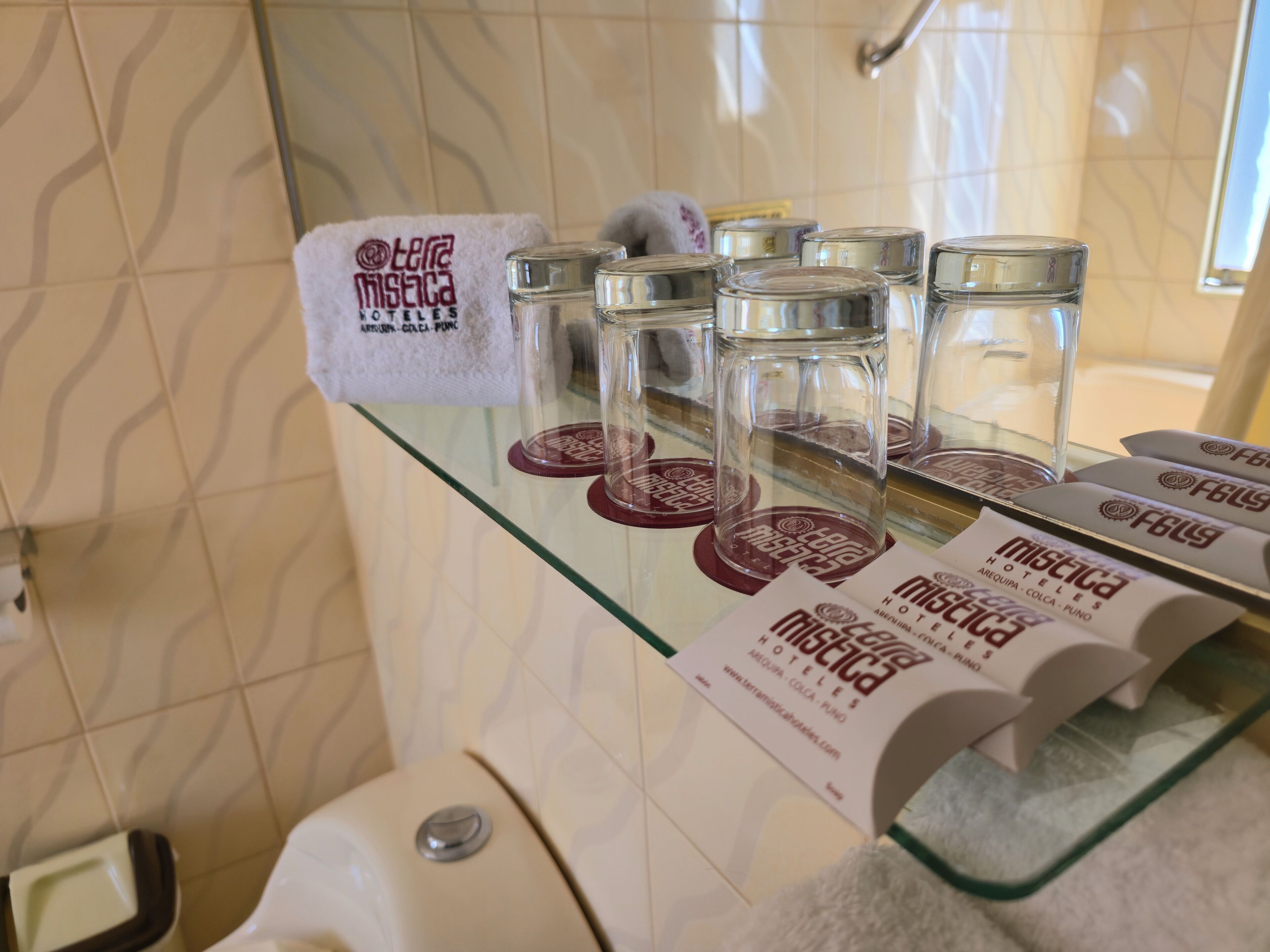 Une salle de bain avec une étagère en verre où sont rangés des articles de toilette, une serviette et un récipient en verre portant une étiquette.