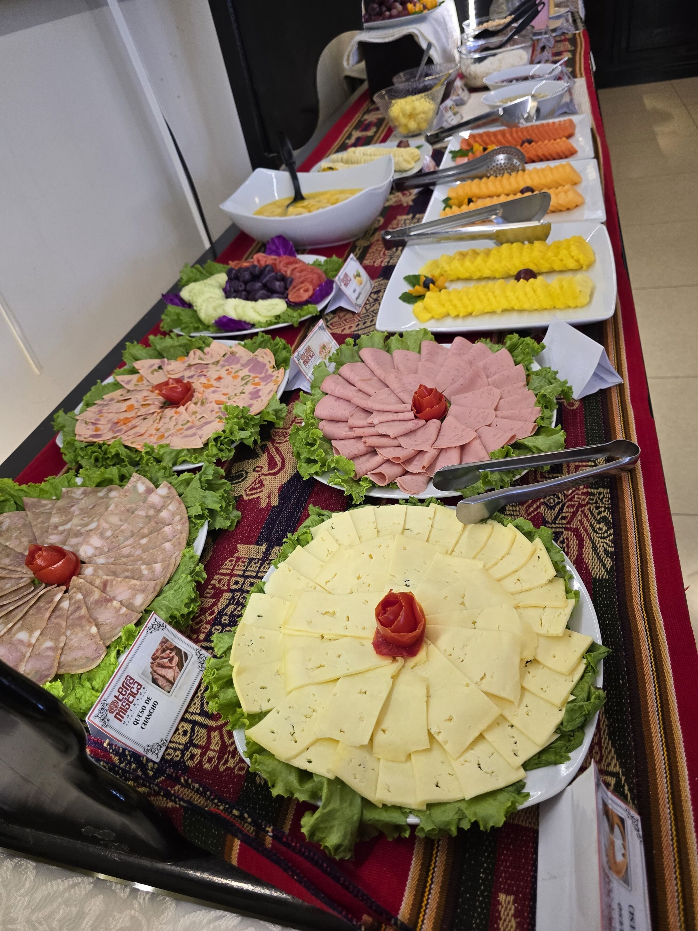 A buffet table with various food items including sliced meats, cheeses, and fruits.