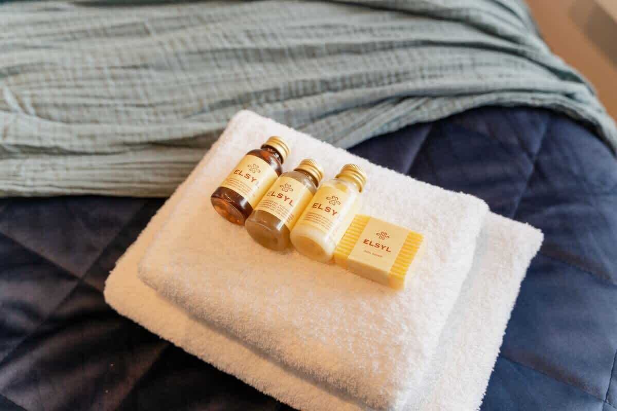 Una cama con una toalla blanca y cuatro botellas de ELSY encima.