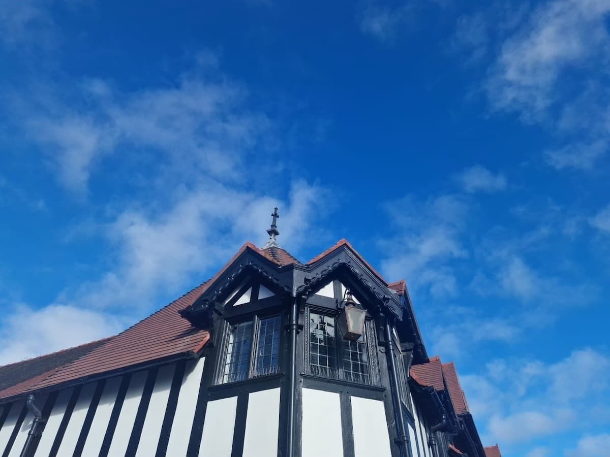 Un edificio con un tejado empinado, una cruz destacada en la cumbre y varias ventanas con marcos blancos.