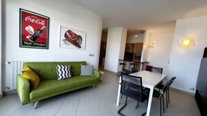 A modern living room with a green sofa, a dining table with chairs, and a kitchen area in the background. - TORRE AZZURRA - SUNSET (Follonica)