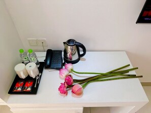 A white table with a black telephone, a silver kettle, two green bottles, two white mugs, a spoon, a packet of tea, and several pink flowers. - Aodai Inn Saigon (Ho Chi Minh City)