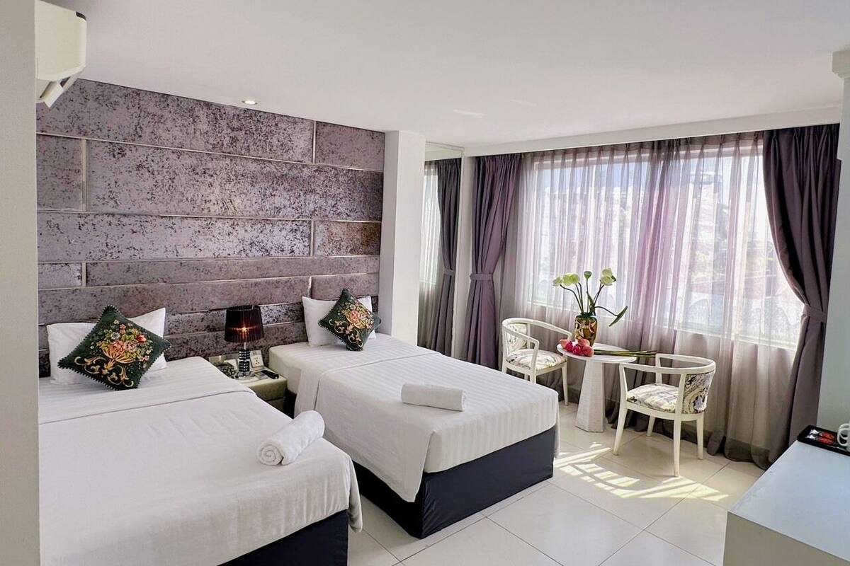 A hotel room with two beds, a small table with chairs, and a large window with curtains.