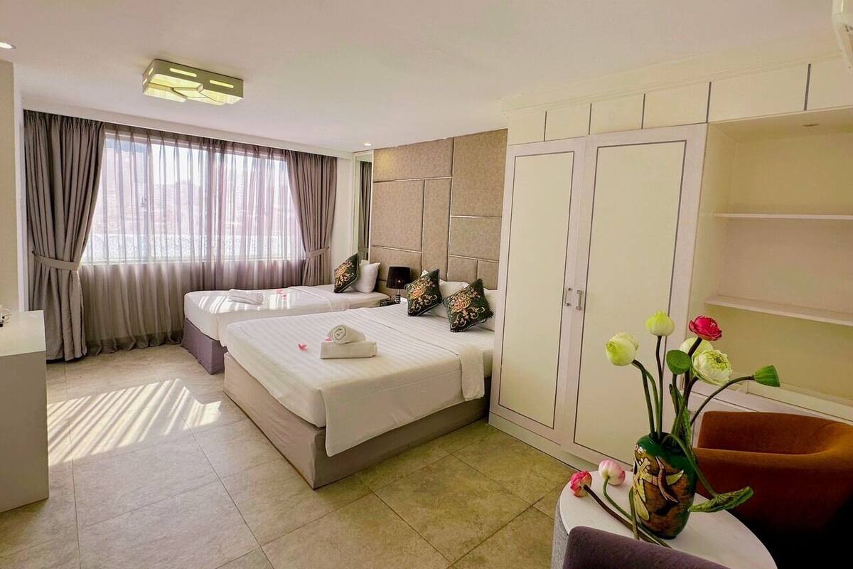 A hotel room with two beds, a wardrobe, a desk, and a vase with flowers.