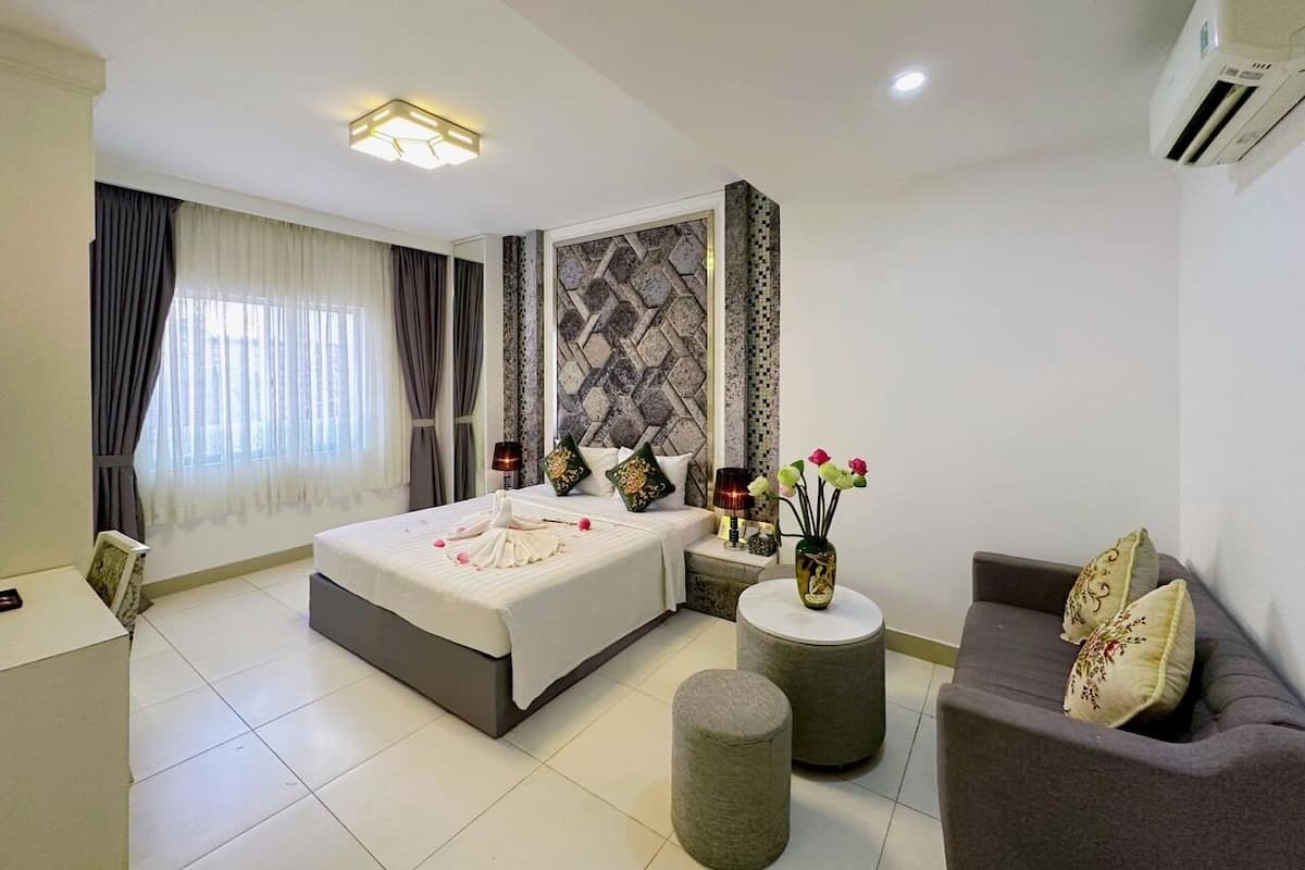 A modern hotel room with a large bed, a sofa, a small table, and a decorative wall.