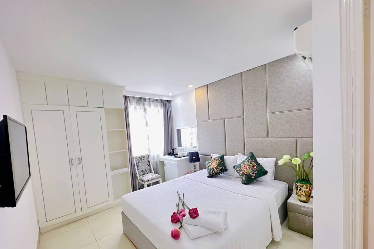 A hotel room with a large bed, a desk, a chair, and a TV mounted on the wall.