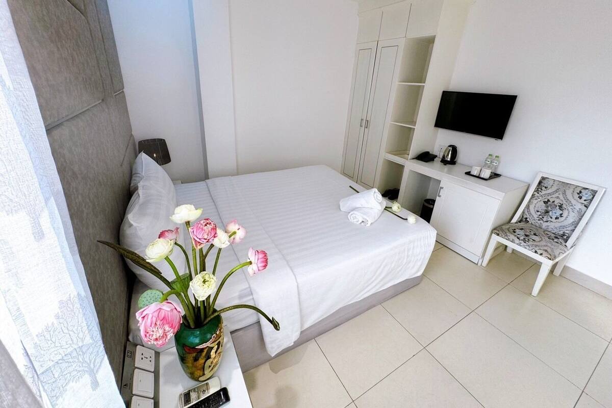 A hotel room with a bed, a TV, a desk with a chair, and a vase of flowers.