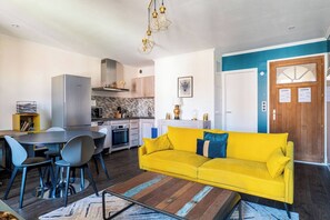 Una cucina moderna con frigorifero, piano cottura e microonde. C'è un tavolo da pranzo con sedie e un divano giallo.
