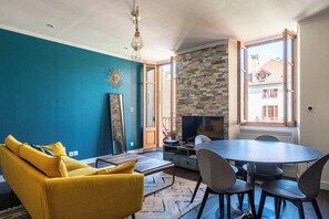 Un salon comprenant un canapé, une table ronde et des chaises, un téléviseur et un mur en pierre.