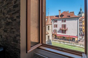 Une fenêtre donnant sur un bâtiment dont le toit est recouvert de tuiles rouges et qui est surmonté d’un clocher.