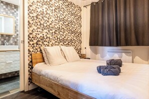 Ein Schlafzimmer mit einer Wand im geometrischen Muster, einem Bett mit Kissen, einem Nachttisch und einem Badezimmer mit gefliesten Wänden und Waschbecken.