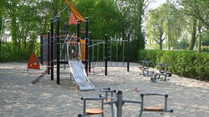 Un parque infantil con varios juegos como toboganes y columpios, rodeado de arena y follaje.