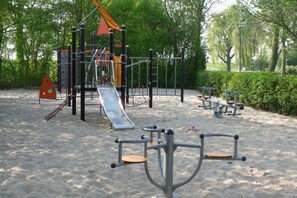 A playground with various equipment like slides and swings, surrounded by sand and greenery. - Holiday Home in Zevenhuizen with Sauna (Zevenhuizen)
