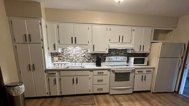 Una cocina con armarios blancos, estufa, microondas y refrigerador.