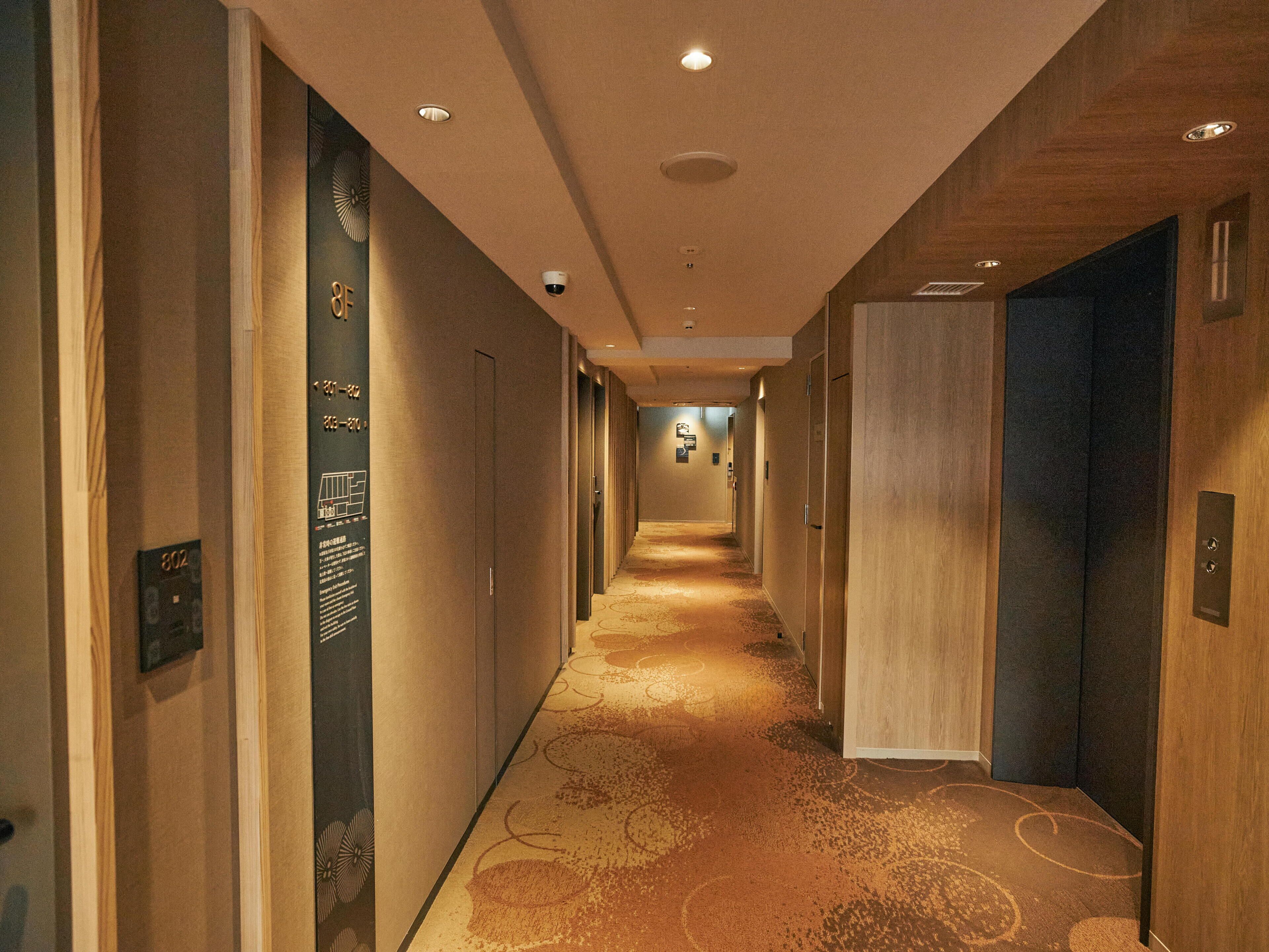 A hotel hallway with carpeted floors, wooden walls, and doors on both sides.