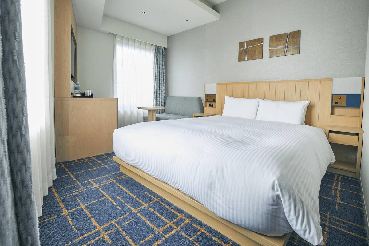 A hotel room with a large bed, a wooden nightstand, a desk, and a wardrobe.