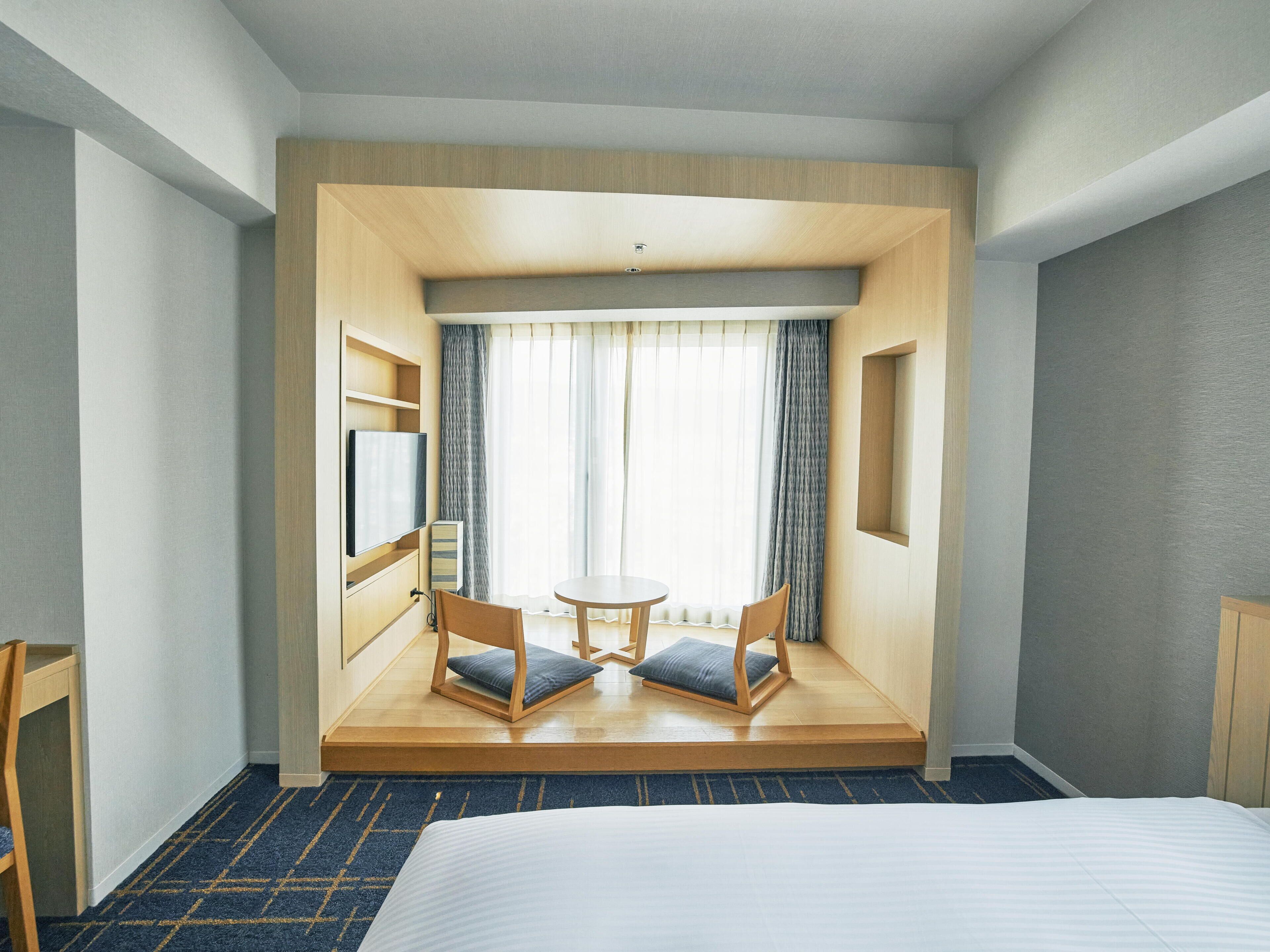 Une chambre d’hôtel avec un lit, une télévision, une petite table avec deux chaises et une fenêtre avec des rideaux.