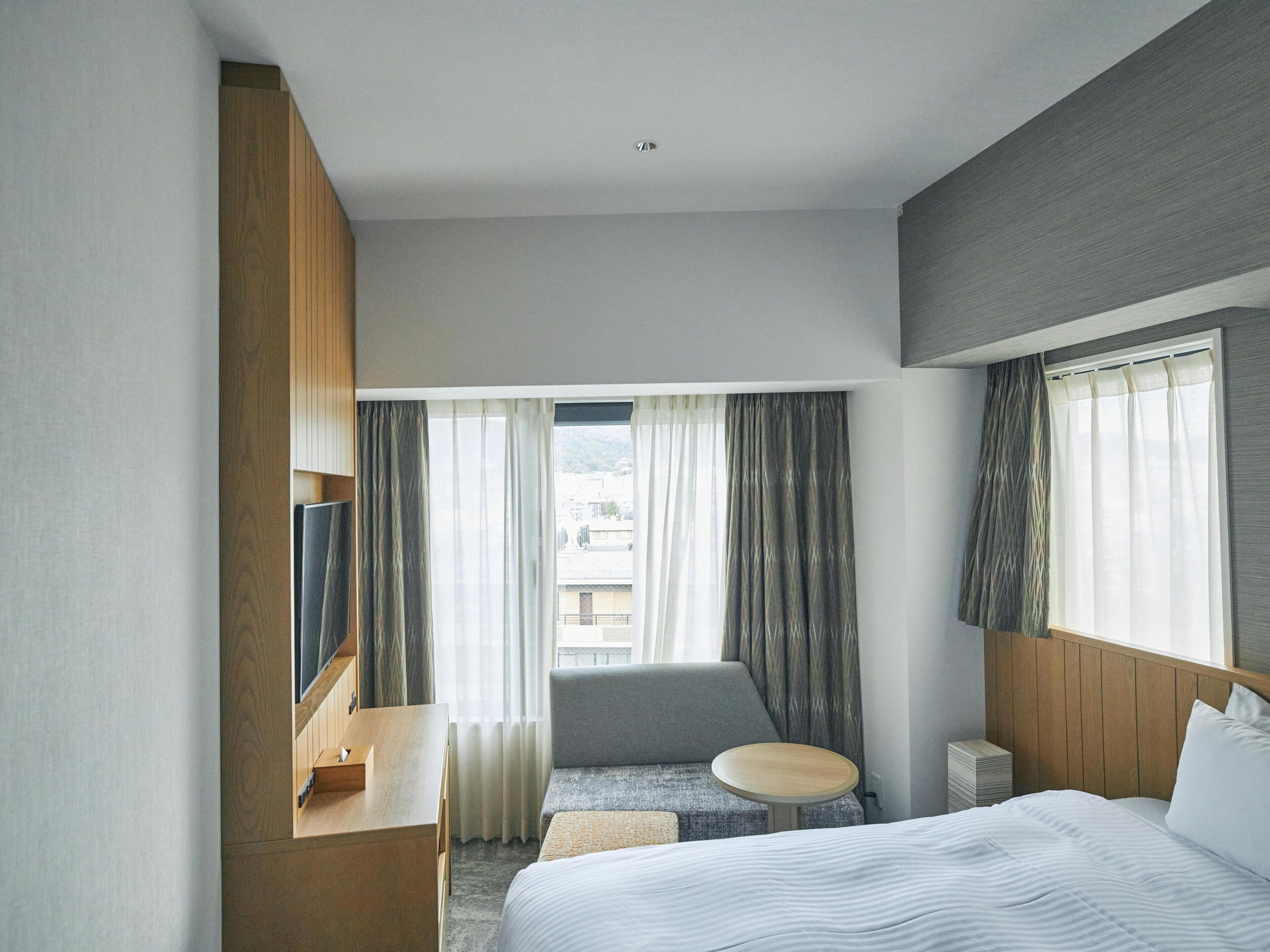 A hotel room with a bed, a seating area, a TV, and a window with curtains.