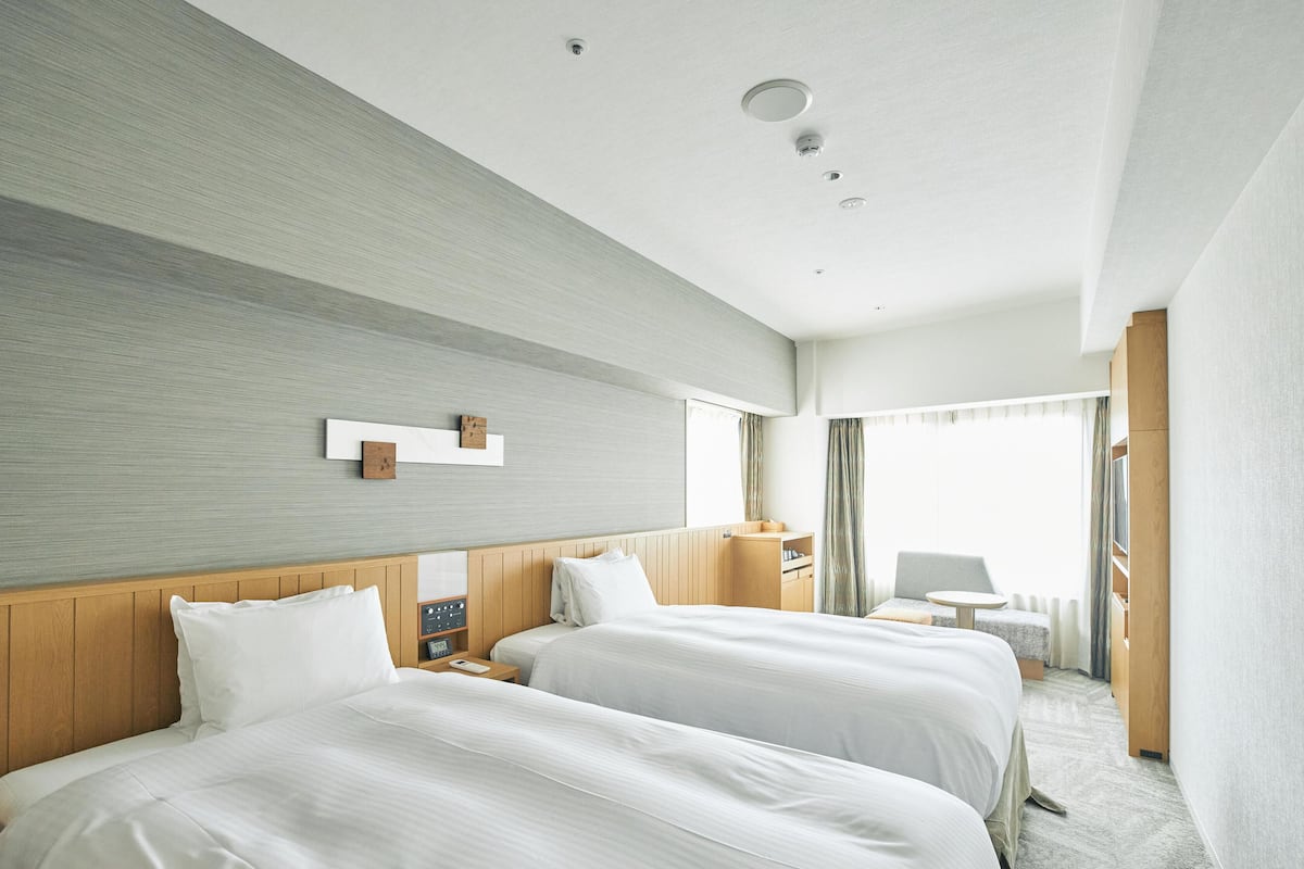 A hotel room with two beds, a wooden headboard, a bedside table, a small desk, and a chair.