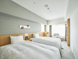A hotel room with two beds, a wooden headboard, a bedside table, a small desk, and a chair.