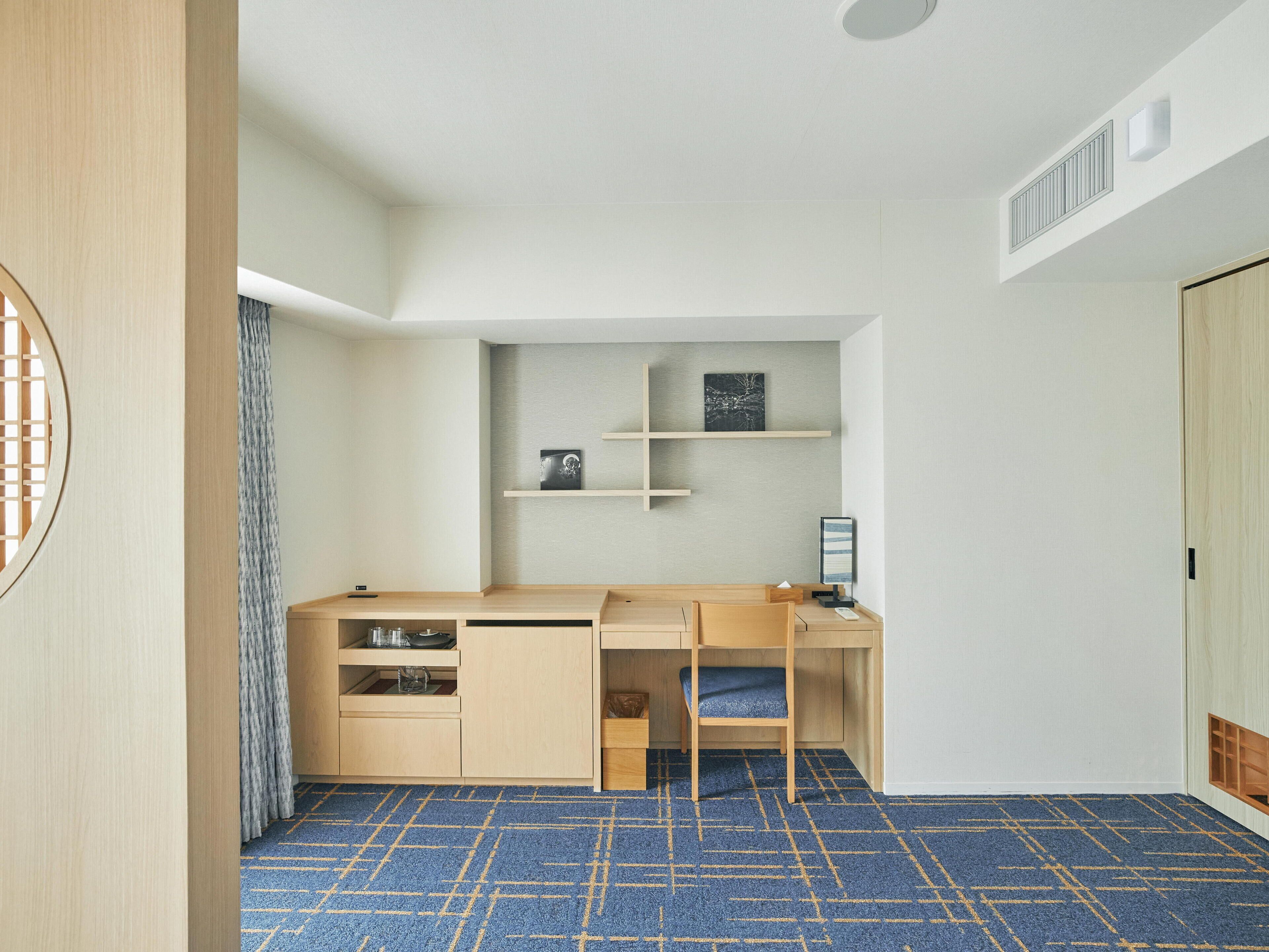 A compact room with a built-in desk, shelving, and a patterned carpet.