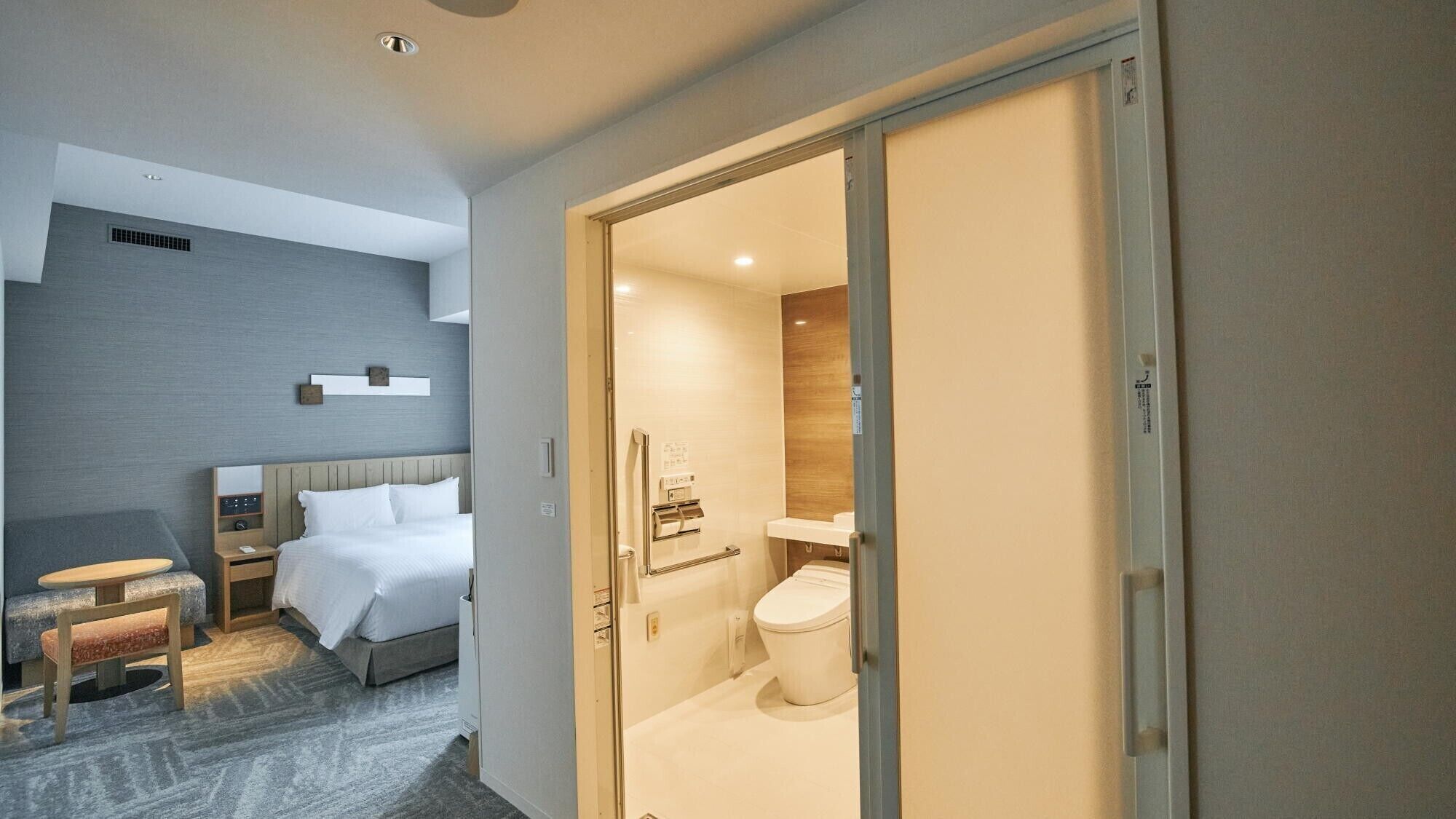 Een hotelkamer met een bed, nachtkastje en een klein zithoekje.