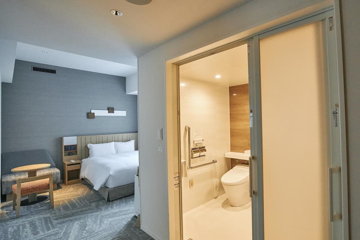 A hotel room with a bed, bedside table, and a small seating area.