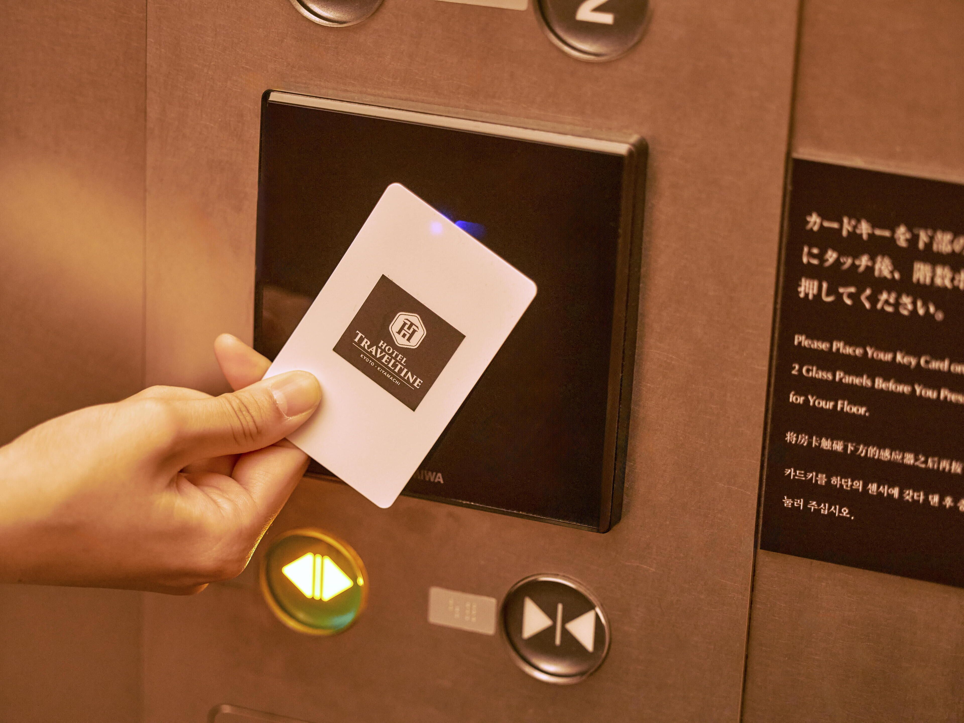 A hand holding a card with a hotel logo, placed in a card reader on an elevator panel.