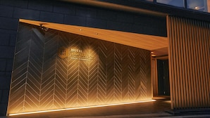 Een hotelentree met een modern ontwerp, met een gevel in een chevronschildering en een houten uitbouw boven de ingang.