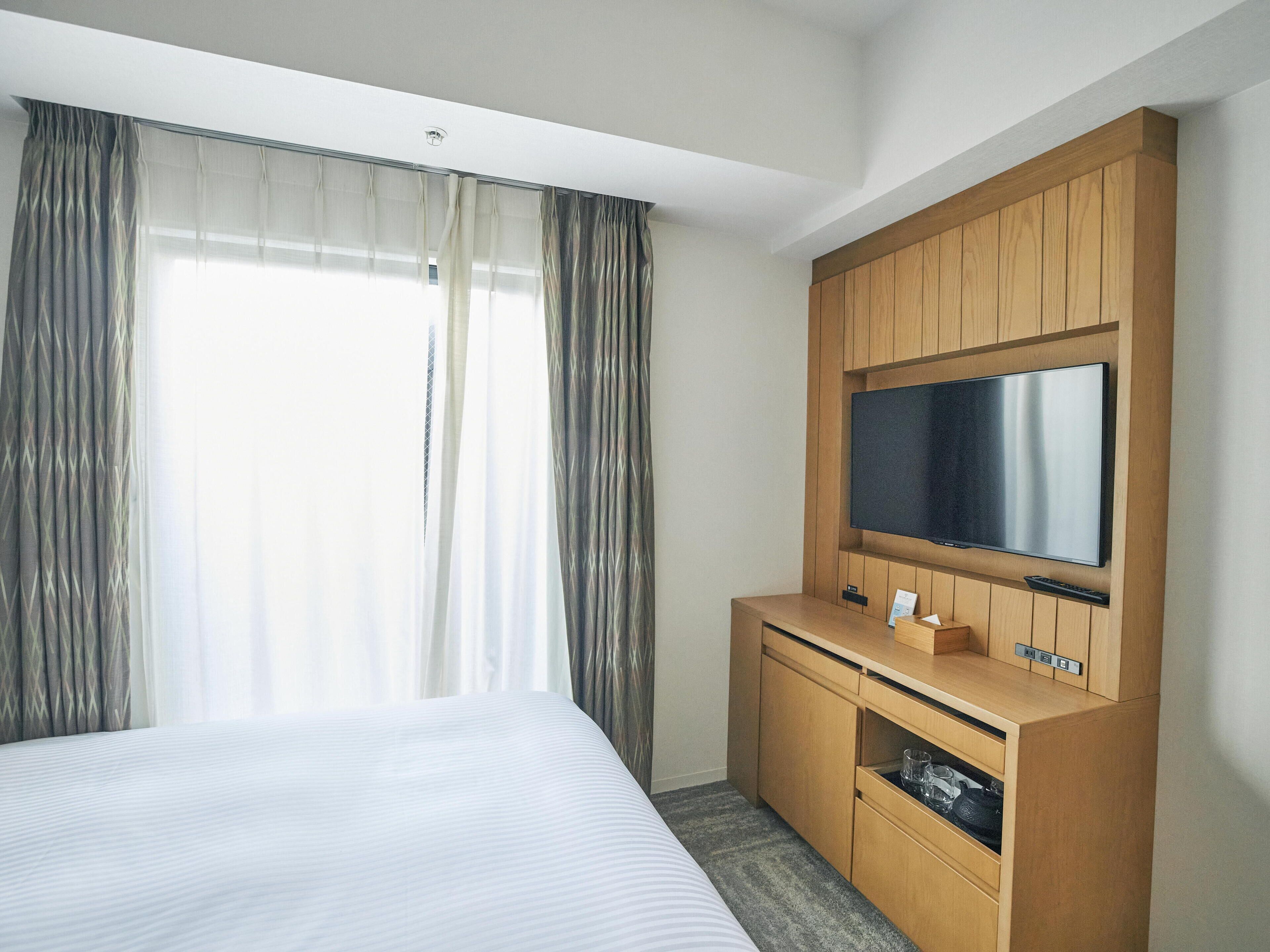 A hotel room with a large bed, a wooden TV stand, and a flat-screen TV.