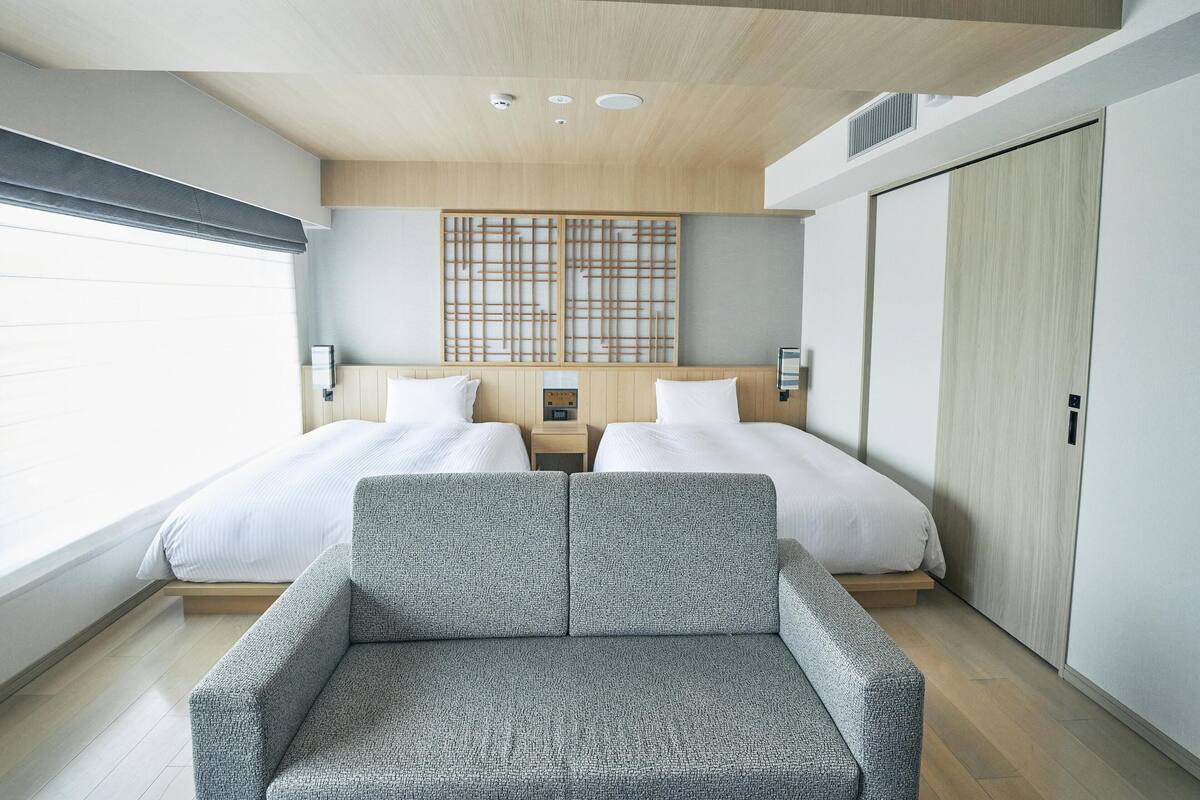 A modern hotel room with two beds, a seating area, and a wooden ceiling.