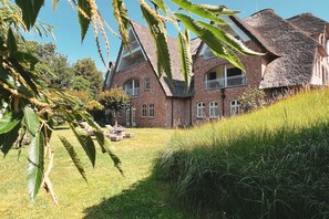 A large brick building with a thatched roof, surrounded by lush greenery and a well-maintained lawn.