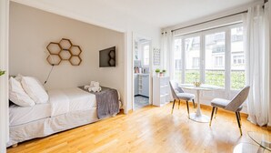 A modern bedroom with a bed, a desk, and a chair. There is a window with curtains, a door leading to a bathroom, and a wall with a geometric decoration. - Palais des Congres - Studio (Paris)