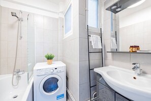 Un baño moderno con lavadora incorporada, bañera, ducha y lavamanos con espejo.