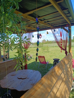 Uma área de estar coberta ao ar livre com mesa e cadeiras, uma rede e vista para um campo gramado.