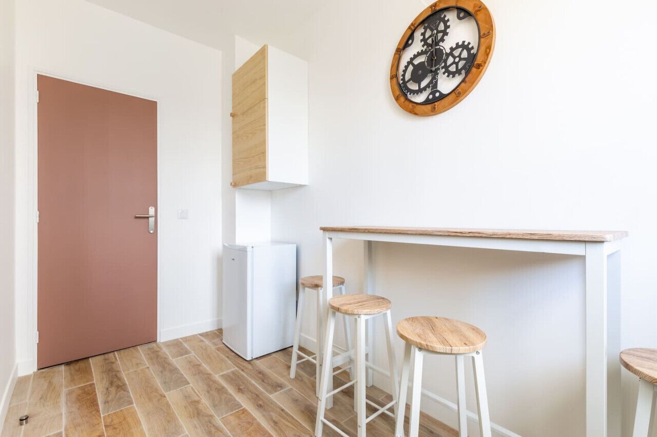 A compact kitchen with a white countertop, two stools, and a wall-mounted clock.