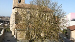 En kirke i sten med et klokketårn og et træ foran.