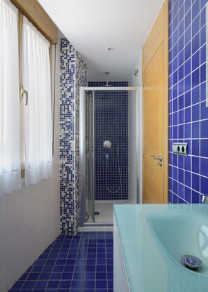 Un bagno con una vasca da bagno in vetro, cabina doccia e pavimento piastrellato.