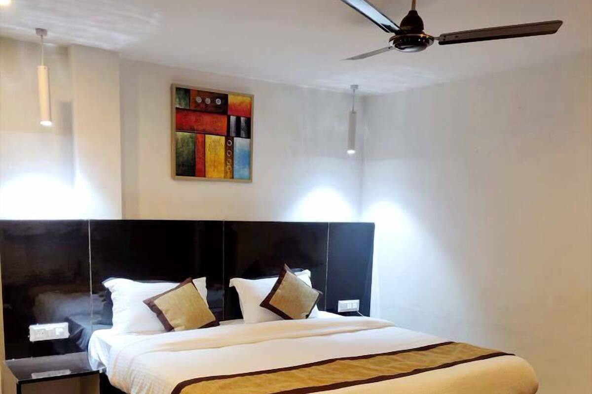 A modern hotel room with a large bed, a ceiling fan, and a painting on the wall.