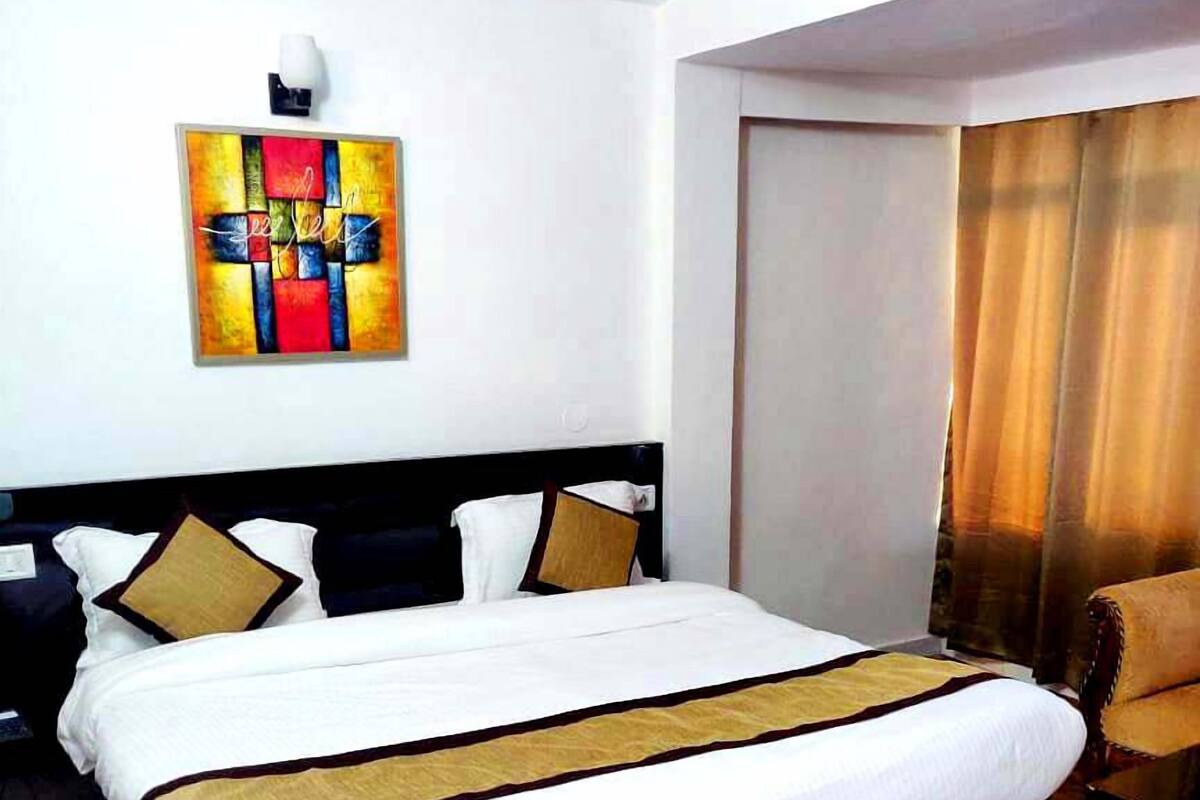 A hotel room with a large bed, a headboard, a nightstand, a lamp, a painting, and a window with curtains.