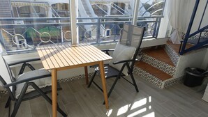 A balcony with a wooden table and chairs, a view of a staircase, and tiled flooring.