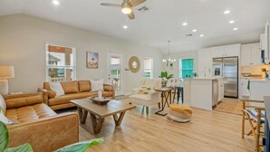 A spacious living room with a sofa, coffee table, and a dining area with chairs. - Sunset Balcony • Covered Patio Lounge + Mins to Beach | Surf-n-dipity (Port Aransas)