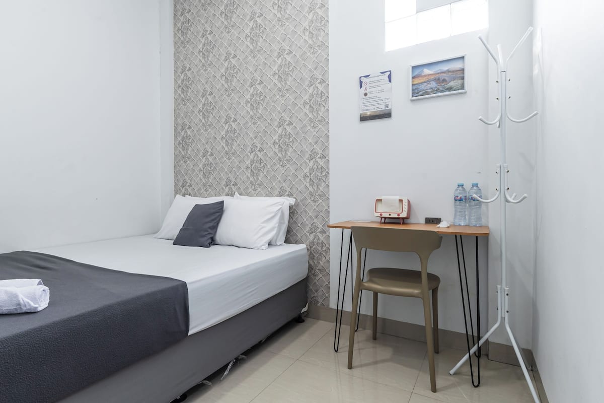 Een hotelkamer met een bed, een bureau, een stoel, een kapstok en een schilderij aan de muur.