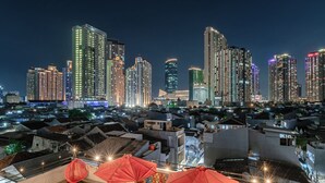 Een stadsbeeld bij nacht met verlichte wolkenkrabbers en een terras op het dak met rode parasols.