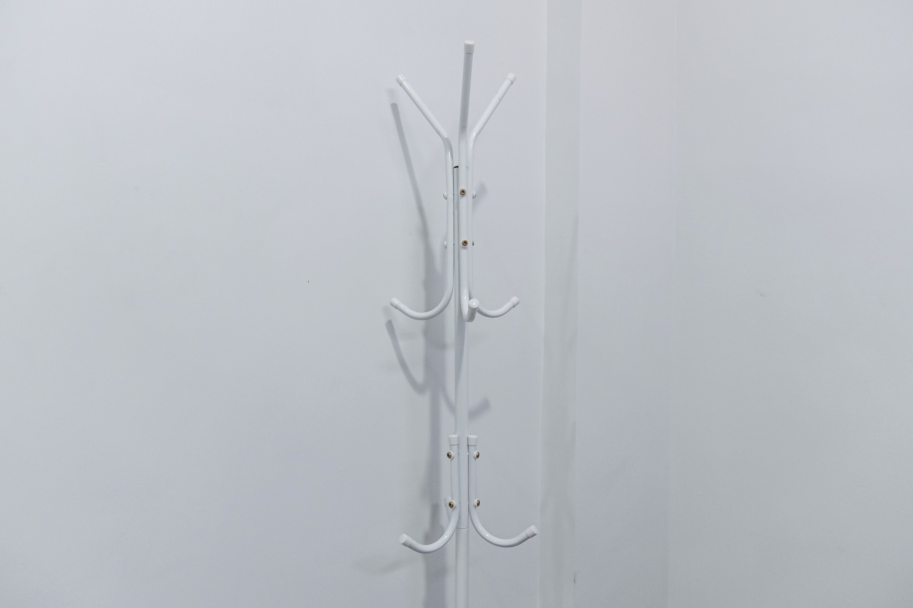 A white coat rack with multiple hooks and pegs against a plain wall.