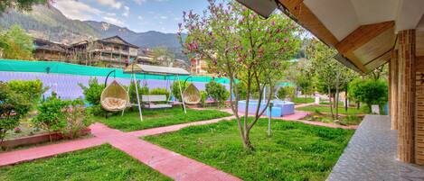 A courtyard with a red brick pathway, hanging chairs, and a small tree with pink flowers.