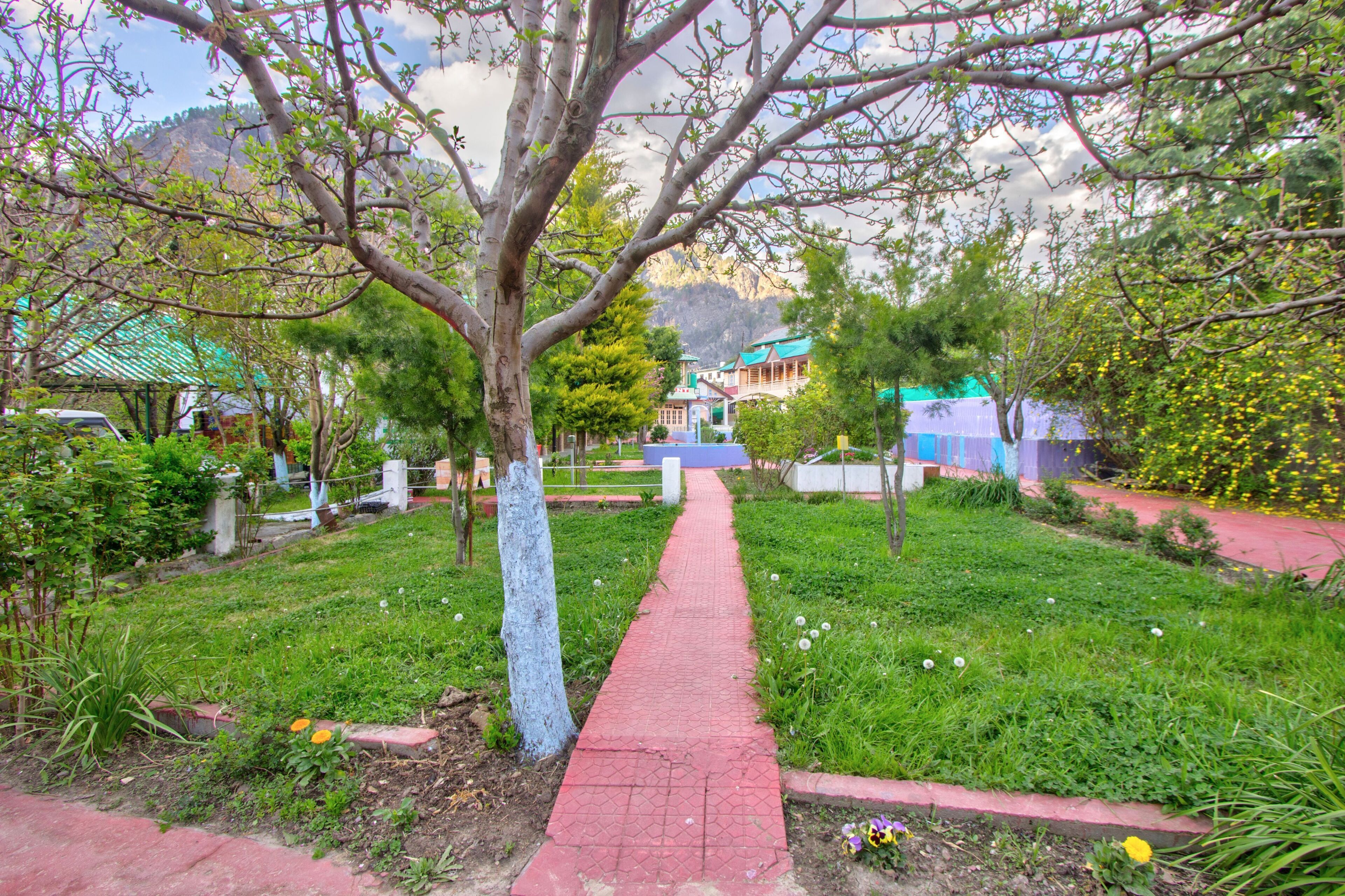 A pathway leading through a garden with trees and a building in the background.