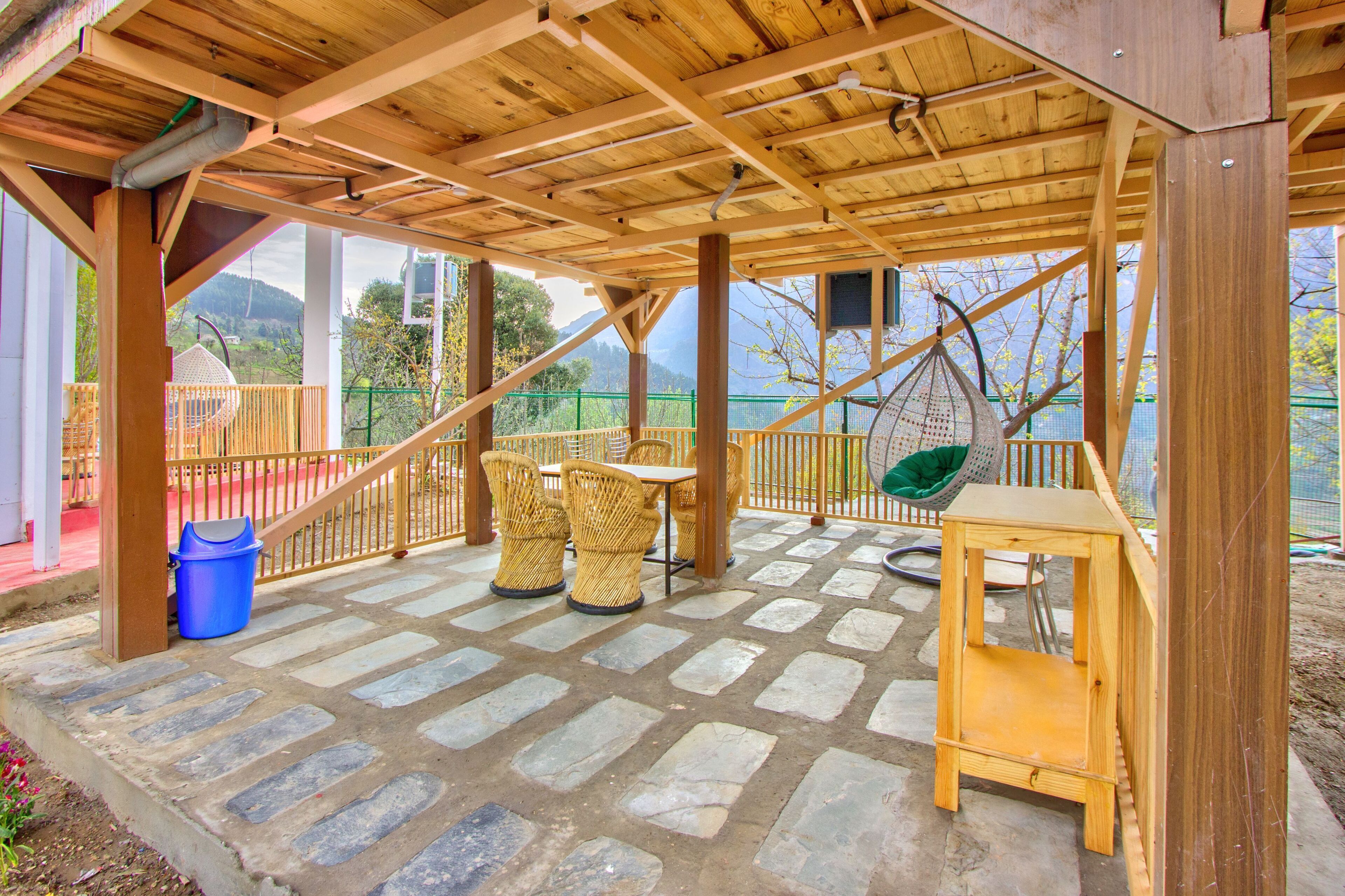 Un patio techado con suelo de piedra, mobiliario de madera y vistas al exterior.